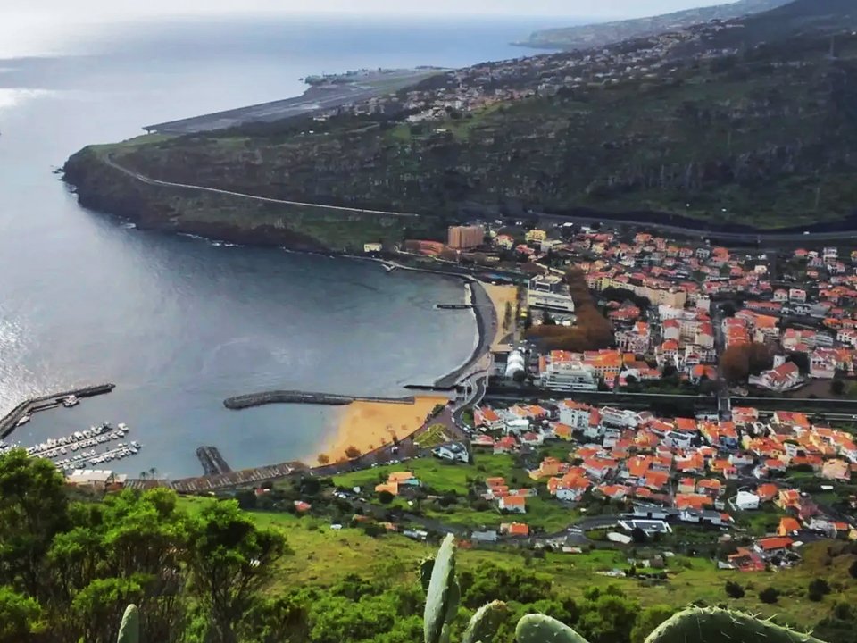Panoramic view over the red rooftops and curved shoreline of Machico from Pico do Facho