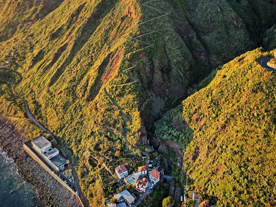 Traditional stone path winding through dry coastal vegetation and volcanic terracing