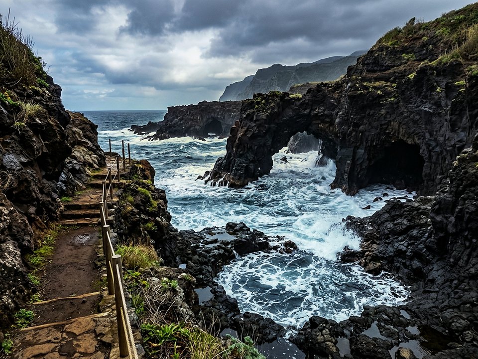 Natural basalt sea caves and weathered volcanic rock arches along the rugged coast of Furnas